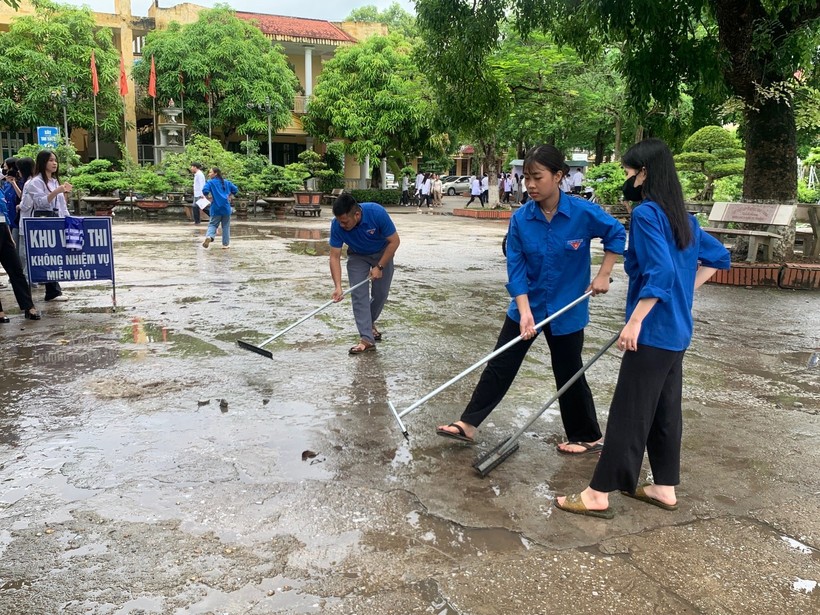 Thanh niên tình nguyện dọn sân tại điểm Trường THPT Chu Văn An để tránh trơn trượt do trời mưa.