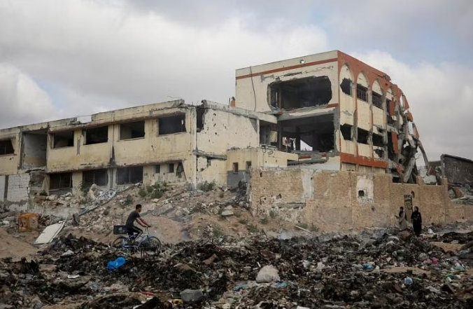 Người Palestine đi ngang qua một ngôi trường bị phá hủy trong cuộc tấn công quân sự của Israel. 