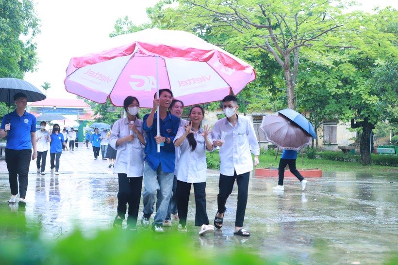 Các thí sinh được thanh niên tình nguyện hỗ trợ che mưa bằng ô cỡ lớn từ cổng vào sân trường. Ảnh: Đình Tuệ.